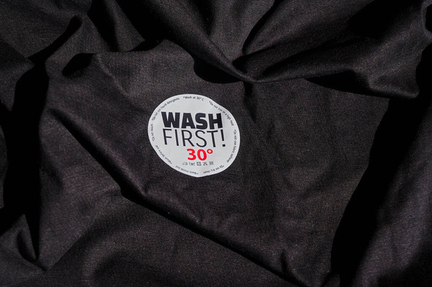 Aufkleber auf einem T-Shirt mit Waschanleitung und dem Text "Wash first". - Foto, Bild