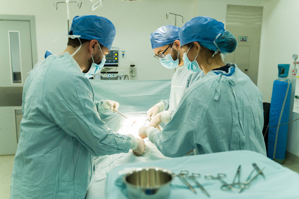 Впевнені хірурги в блакитних скрабах використовують хірургічні інструменти і намагаються врятувати життя пацієнта
 - Фото, зображення