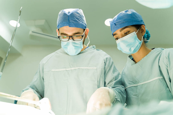 Caucasian surgeon with gloves and scrubs performing surgery with the help of a medical nurse  - Foto, Imagen