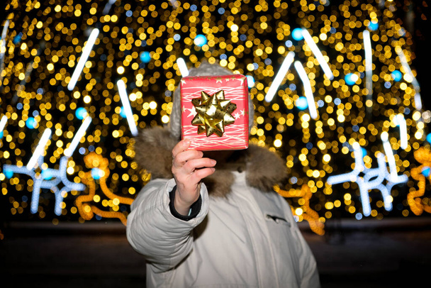 Žena drží červenou krabici s dárkem místo hlavy stojící u vánočního stromku se žlutým věncem - Fotografie, Obrázek