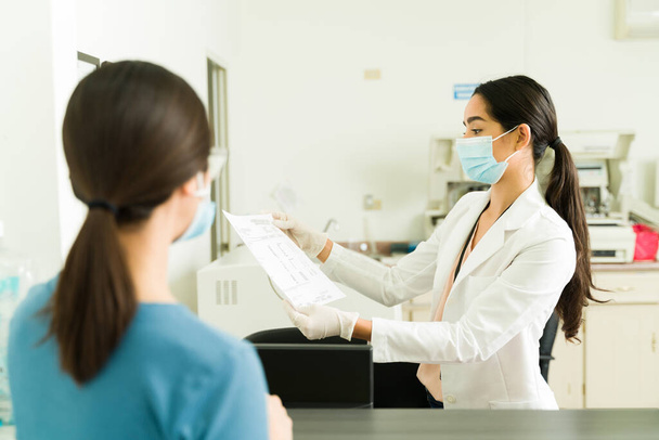 Жінка-помічник з маскою для обличчя дає медичні результати пацієнту в медичній лабораторії
 - Фото, зображення