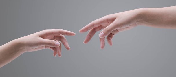 Female hands reaching each other on gray background, spirituality and connection concept - Photo, image