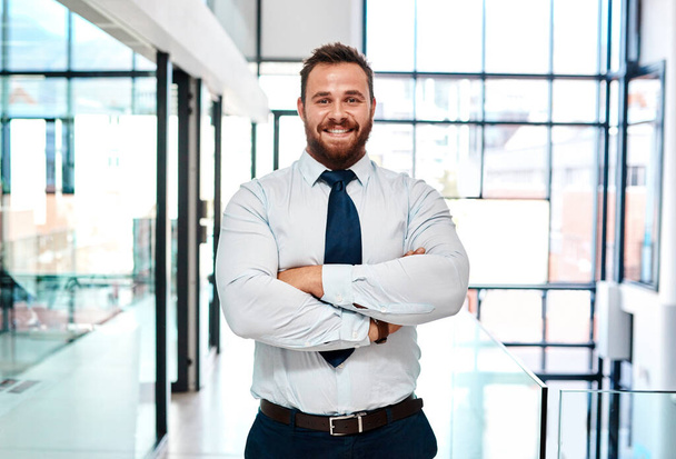 A successful entrepreneur believes in his abilities. Portrait of a young businessman standing with his arms crossed in an office. - Foto, imagen