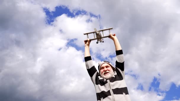Gelukkig grijsaard man doen alsof vliegen op houten vliegtuig in de lucht, reizen - Video