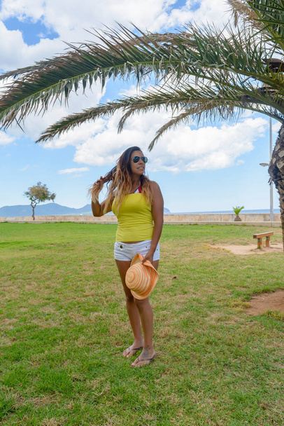 retrato de una mujer latina sonriendo, divirtiéndose, de vacaciones en mallorca posando en un cálido día de primavera y verano, bajo una palmera, concepto de vacaciones - Foto, imagen