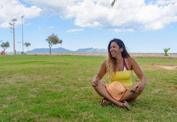 όμορφη Λατίνα γυναίκα 40 ετών, χαμογελώντας κάθεται στο γρασίδι ενός πάρκου στη Μαγιόρκα, βαληρικά νησιά, ολιντικές έννοιες - Φωτογραφία, εικόνα