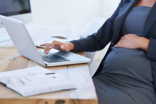 Працюємо заради майбутнього малюка. Обрізане зображення вагітної бізнес-леді, що працює на її ноутбуці в офісі
. - Фото, зображення