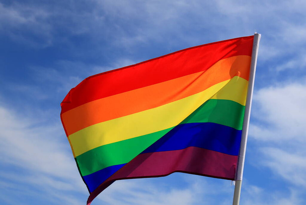 Realistic rainbow flag of an LGBT organization waving against a blue sky. LGBT pride flags include lesbians, gays, bisexuals and transgender people. - Photo, Image