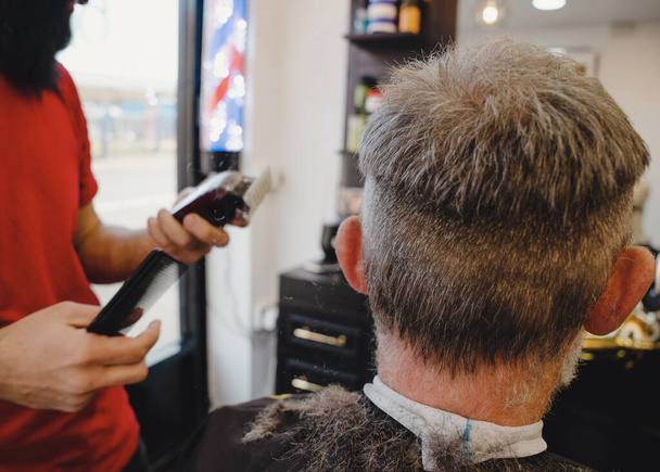 Borbély vágás és vágás szakállas ember borotválkozó gép a fodrászatban. Hajformázási folyamat. - Fotó, kép