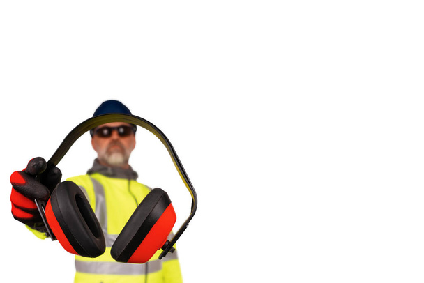 Pracownik budowlany w płaszczu hi-viz i czarne rękawice ochronne dające ochronę ucha widzom odizolowanym na białym tle. Bezpieczeństwo na placu budowy koncepcja banera - Zdjęcie, obraz