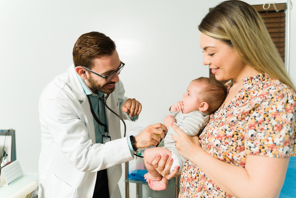 Ευτυχισμένη μητέρα κυοφορεί το υγιές μωρό της ενώ ο άντρας παιδίατρος κάνει μια ιατρική εξέταση.  - Φωτογραφία, εικόνα