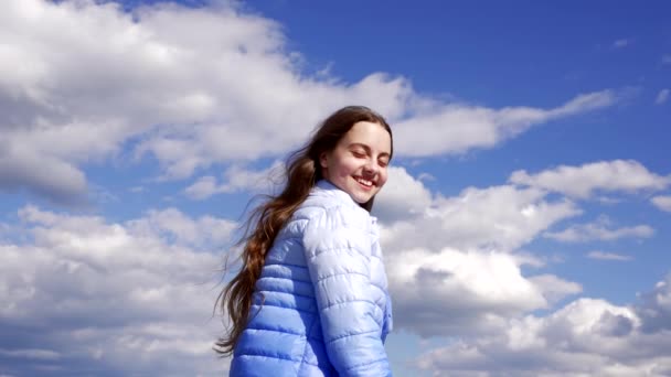 szczęśliwe dziecko z długimi włosami w jesiennej kurtce cieszyć się słońcem na tle nieba, pielęgnacja włosów - Materiał filmowy, wideo