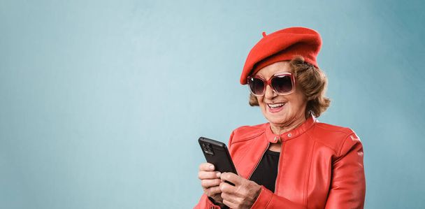 Stilvolle Seniorin lächelt, während sie ihr Mobiltelefon über einem isolierten Hintergrund benutzt. - Foto, Bild
