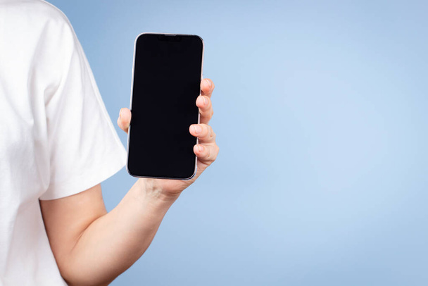 Woman with white t-shirt holding cell phone in her hand and showing smartphone screen direct to camera. Front view - Photo, Image