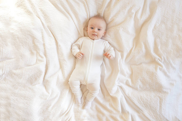 bébé sur une couverture blanche. Bébé couché sur une couverture de mousseline blanche sur le sol, regardant la caméra. - Photo, image