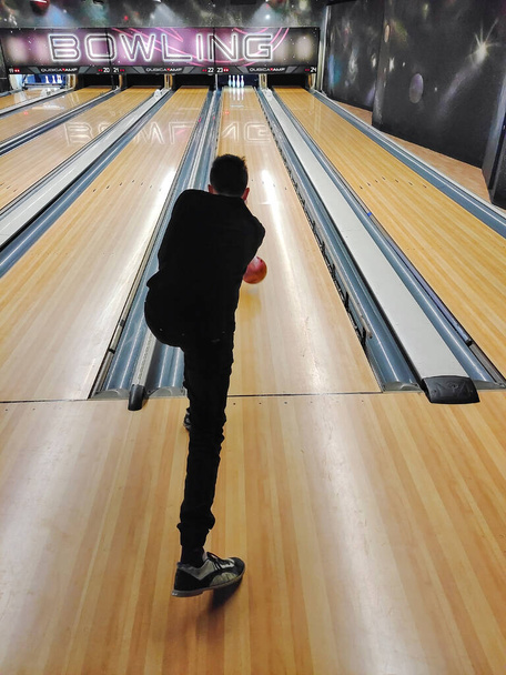Guy Teenager spielt Bowling, schwingt und wirft den Ball in die Kegel. Blick zurück in die Perspektive - Foto, Bild