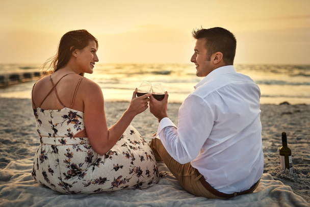 Ad una serata davvero perfetta. Retrovisore di una giovane coppia affettuosa che si gode un po 'di vino seduti sulla spiaggia. - Foto, immagini