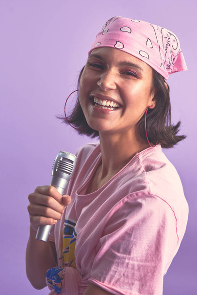 Tervehtikää karaokekuningatarta. Studio laukaus kaunis nuori nainen laulaa mikrofoni vastaan violetti tausta. - Valokuva, kuva