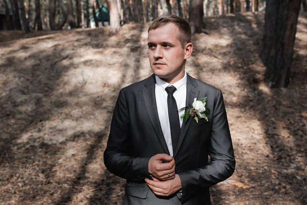 Elegante bruidegom in een zwart pak in een dennenbos. Een man van Slavisch uiterlijk. - Foto, afbeelding