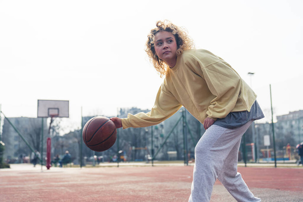 Pretty Caucasian woman bends down while playing basketball on the sports field medium full shot copy space  - Zdjęcie, obraz