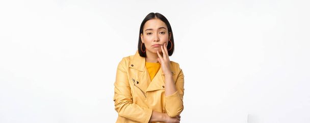 Image of stylish japanese girl looking with unamused, tired and upset face expression, standing in casual clothes over white background - Foto, Imagem