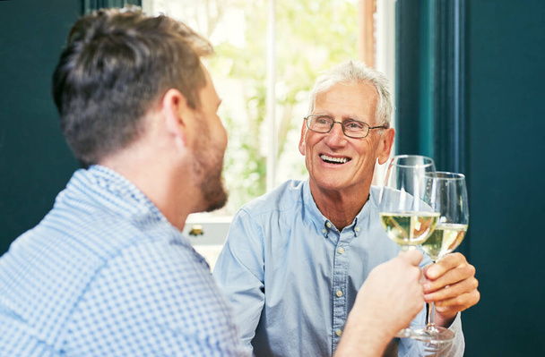 Heres to you and me dad. Shot of a cheerful elderly man and his son sharing a celebratory toast with wine glasses at home. - Фото, изображение