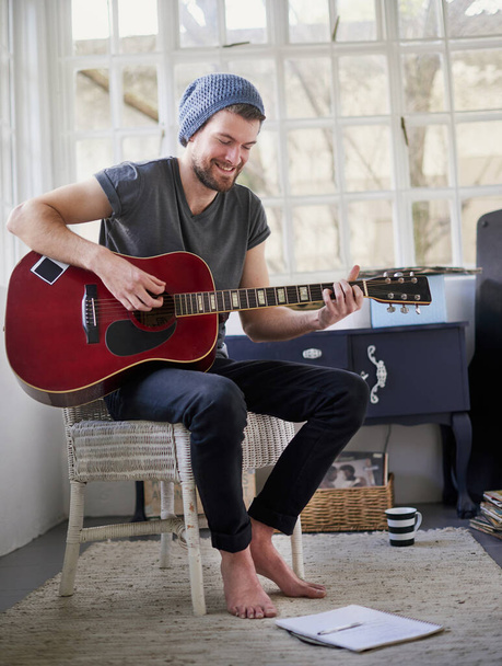 Practising for his upcoming solo performance. Shot of a handsome young man playing a guitar at home. - Foto, afbeelding