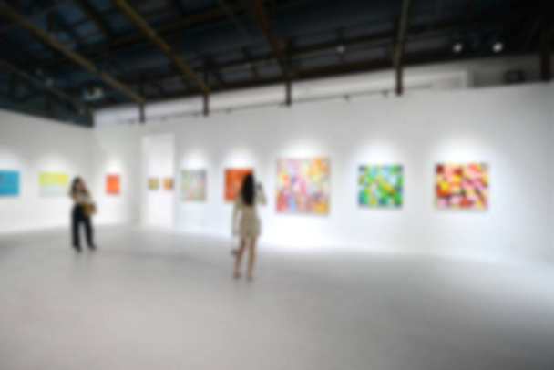 People looking at paintings on white wall in Art exhibition gallery. Blurry background. - Photo, Image