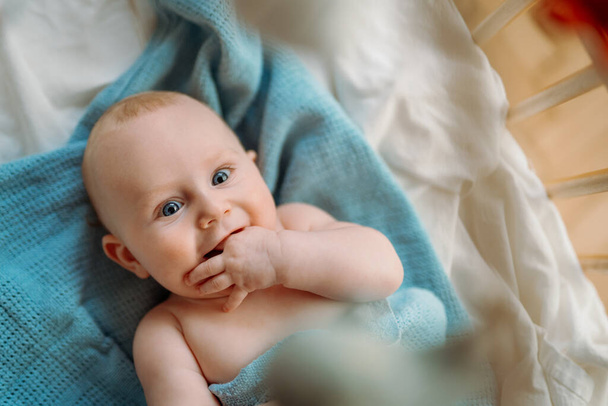 Bambino bambino sdraiato sulla coperta blu, sorridente e distogliendo lo sguardo. Foto di copertina - Foto, immagini