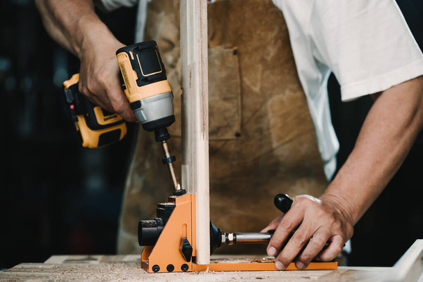 Tischler verwenden Bohrer und Zentrierdübelvorrichtung oder Taschenlochvorrichtung, um starke Verbindungen auf Holzplatte herzustellen. Holzbearbeitungskonzept. Selektiver Fokus. - Foto, Bild