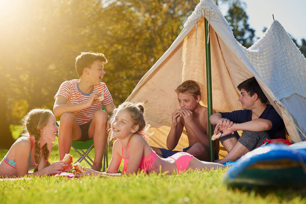 El verano pertenece a los jóvenes. Fotografía de un grupo de jóvenes amigos pasando el rato en su campamento. - Foto, imagen