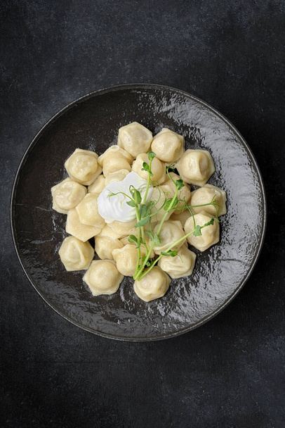 Ukrainian dumplings with sour cream, on a black glossy plate, on a dark background - Photo, Image