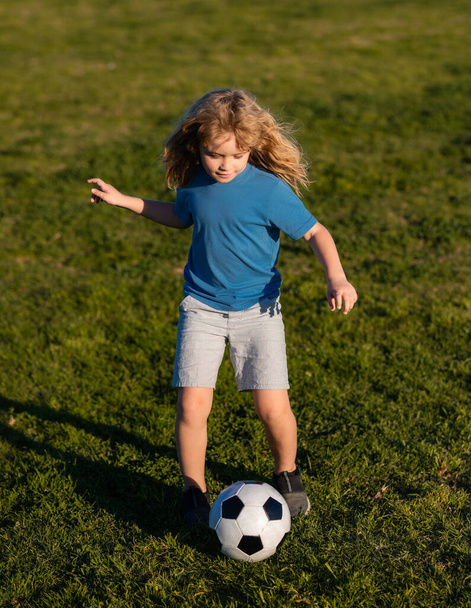 Soccer kid boy playing football. Child boy play football on outdoor field. Children score goal at soccer game. Kid kicking a football ball on a grass. - Фото, изображение