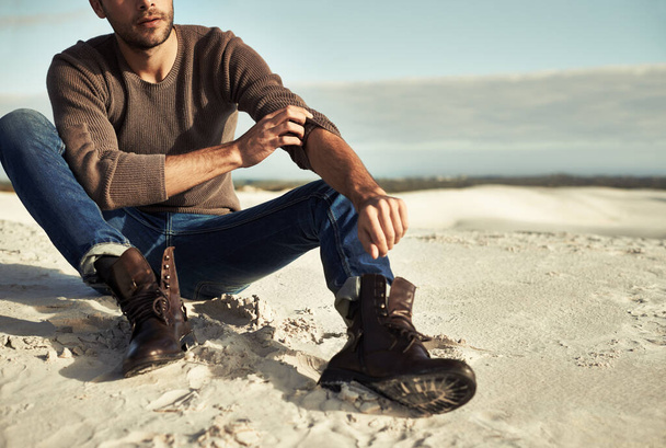 Momentos junto al mar. Un hombre con jeans y botas sentado en la playa. - Foto, imagen