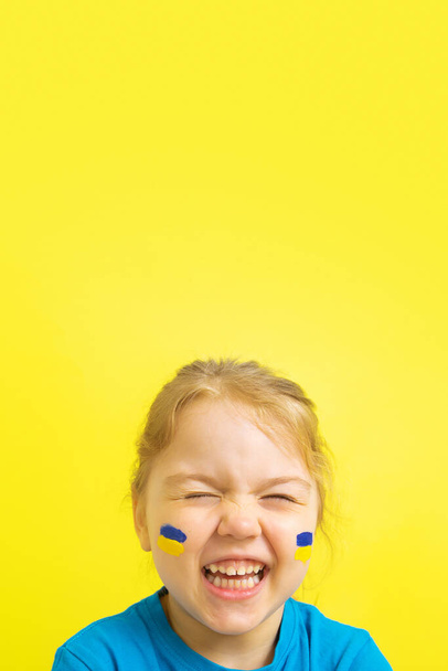 Sorridente ragazza felice con una bandiera ucraina dipinta di giallo e blu sulle guance. Foto verticale con spazio di copia.  - Foto, immagini