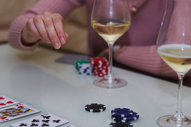 Kobieta wykonuje ruch w grze w pokera. Chipsy, karty, kieliszki szampana na stole z odbiciem. Fotografia w stylu życia - Zdjęcie, obraz