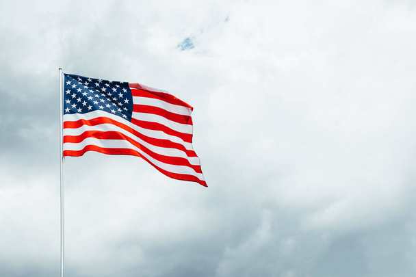USA Amerika vlag wapperend in de wind boven bewolkte lucht. - Foto, afbeelding
