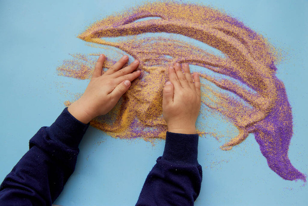 Το μωρό παίζει με πολύχρωμη άμμο. Ανάπτυξη κινητικών δεξιοτήτων παιδιών. Δημιουργικό επάγγελμα για παιδιά. Άποψη από ψηλά - Φωτογραφία, εικόνα