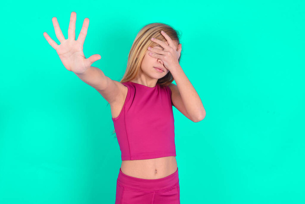 little caucasian kid girl  covers eyes with palm and doing stop gesture, tries to hide. Don't look at me, I don't want to see, feels ashamed or scared. - Photo, Image