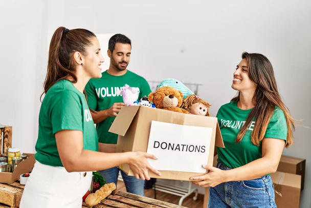 Группа латиноамериканских добровольцев улыбается счастливой держащей коробку с игрушками для пожертвования в благотворительном центре. - Фото, изображение