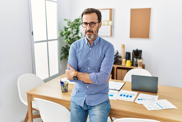 Middle age hispanic man with beard wearing business clothes at the office skeptic and nervous, disapproving expression on face with crossed arms. negative person.  - Фото, изображение