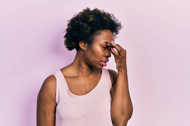 Young african american woman wearing casual sleeveless t shirt tired rubbing nose and eyes feeling fatigue and headache. stress and frustration concept.  - Photo, Image