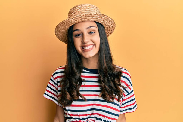 Junge hispanische Frau mit Sommerhut sieht positiv und glücklich stehend aus und lächelt mit einem selbstbewussten Lächeln, das Zähne zeigt  - Foto, Bild