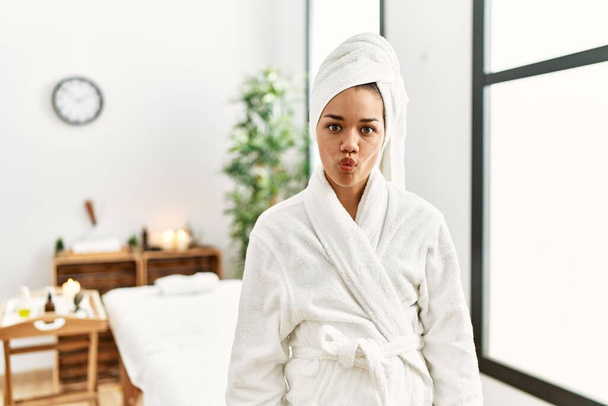 Young brunette woman wearing towel and bathrobe standing at beauty center making fish face with lips, crazy and comical gesture. funny expression.  - Foto, Imagem