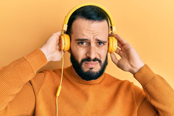 Young man with beard listening to music using headphones skeptic and nervous, frowning upset because of problem. negative person.  - Foto, Imagem