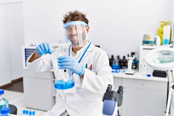 Mladý hispánec muž na sobě vědec uniforma držení zkumavky v laboratoři - Fotografie, Obrázek