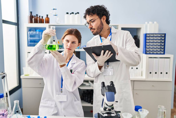 Erkek ve kadın bilim adamı partnerler laboratuardaki panoda test tüpü yazıları tutuyor. - Fotoğraf, Görsel