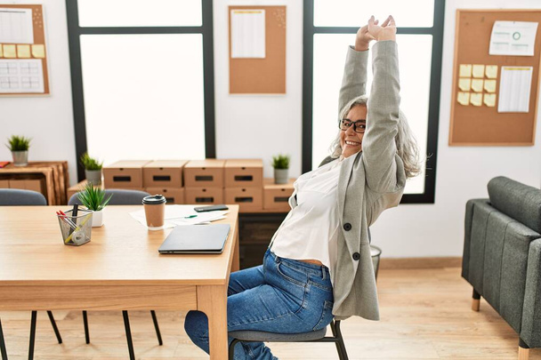 Middle age grey-haired businesswoman tired stretching arms working at the office. - Foto, Imagen