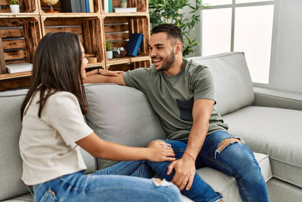 Joven pareja latina conversando sentada en el sofá de su casa. - Foto, Imagen