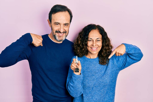 Pár hispánských žen středního věku a muž držící klíče od nového domova, který vypadá sebevědomě s úsměvem na tváři, ukazuje na sebe hrdými a šťastnými prsty.  - Fotografie, Obrázek